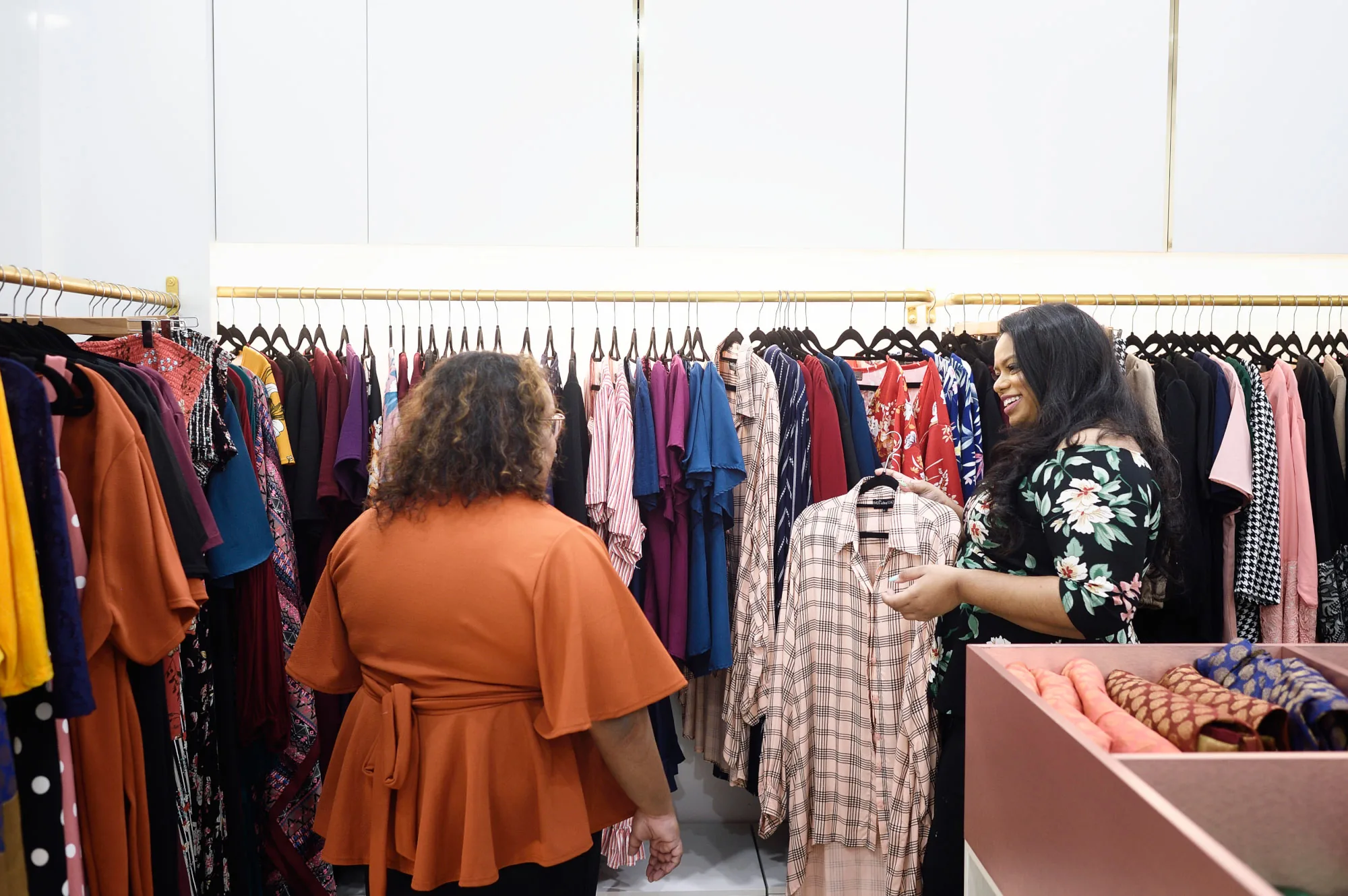 Rani holding up a checked shirt for a client, seen from behind, in front of a rail of colourful dresses