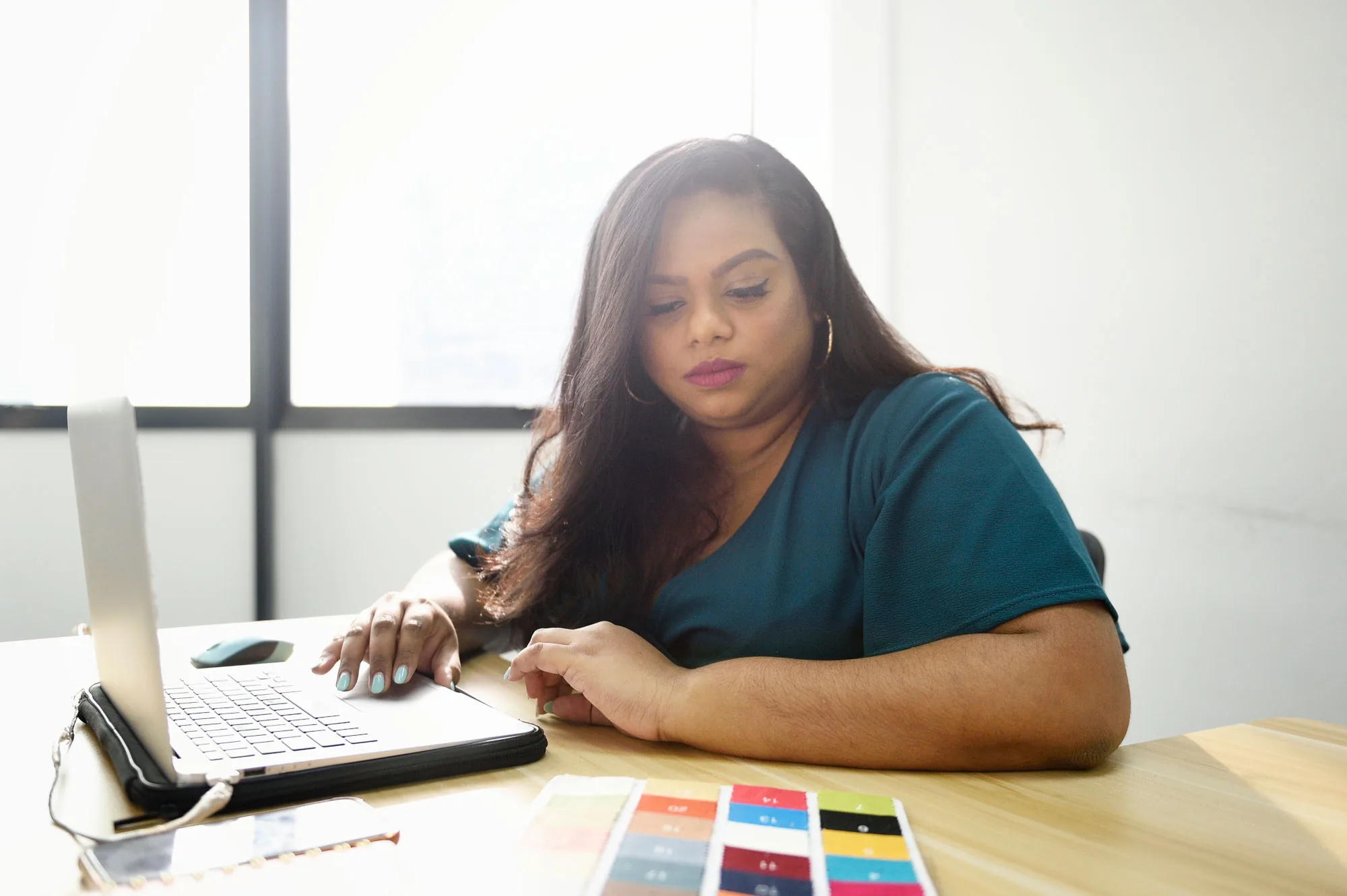 Rani at a desk with her laptop and a card of colour swatches, looking down at her work