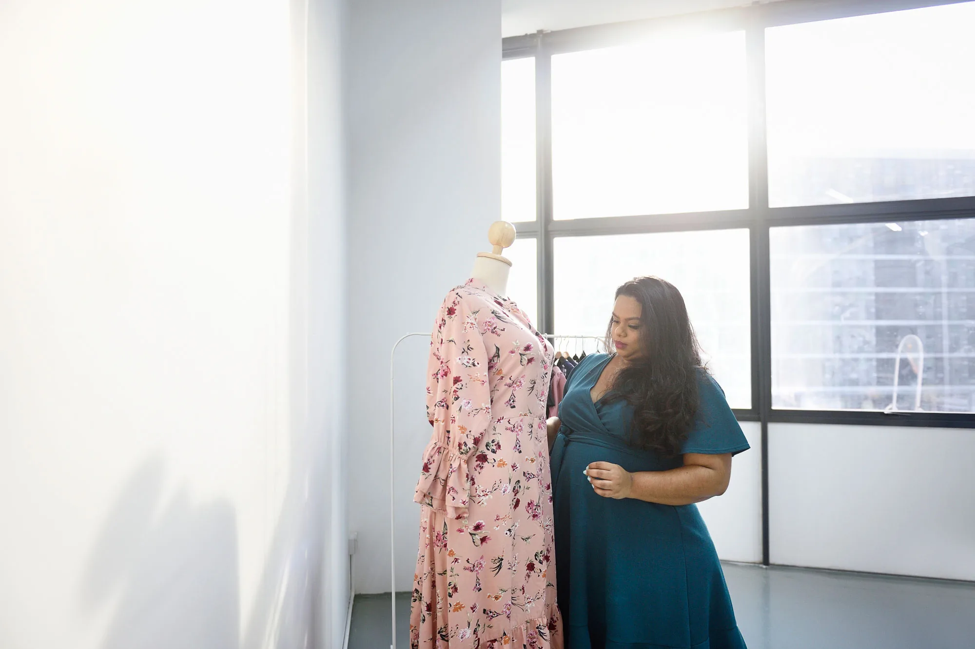 Rani considering a floral dress on a mannequin beside a tall studio window